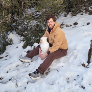 A man sitting in the snow, making a snowman wearing a winter jacket. 