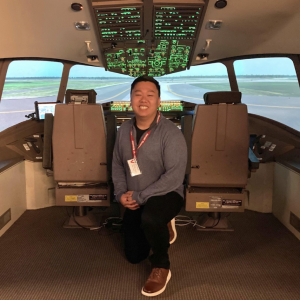 A man kneeling in front of a pilots cockpit smiling.