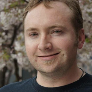 A man smiling in front of flowering trees.